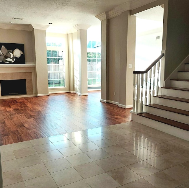 unfurnished living room featuring visible vents, crown molding, stairs, a fireplace, and a textured ceiling