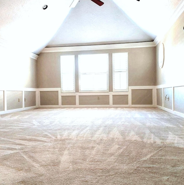 empty room featuring a ceiling fan, a healthy amount of sunlight, carpet, lofted ceiling, and ornamental molding