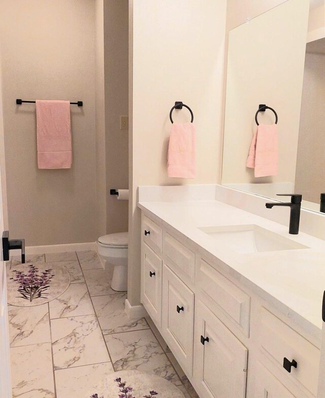 bathroom with vanity, toilet, baseboards, and marble finish floor