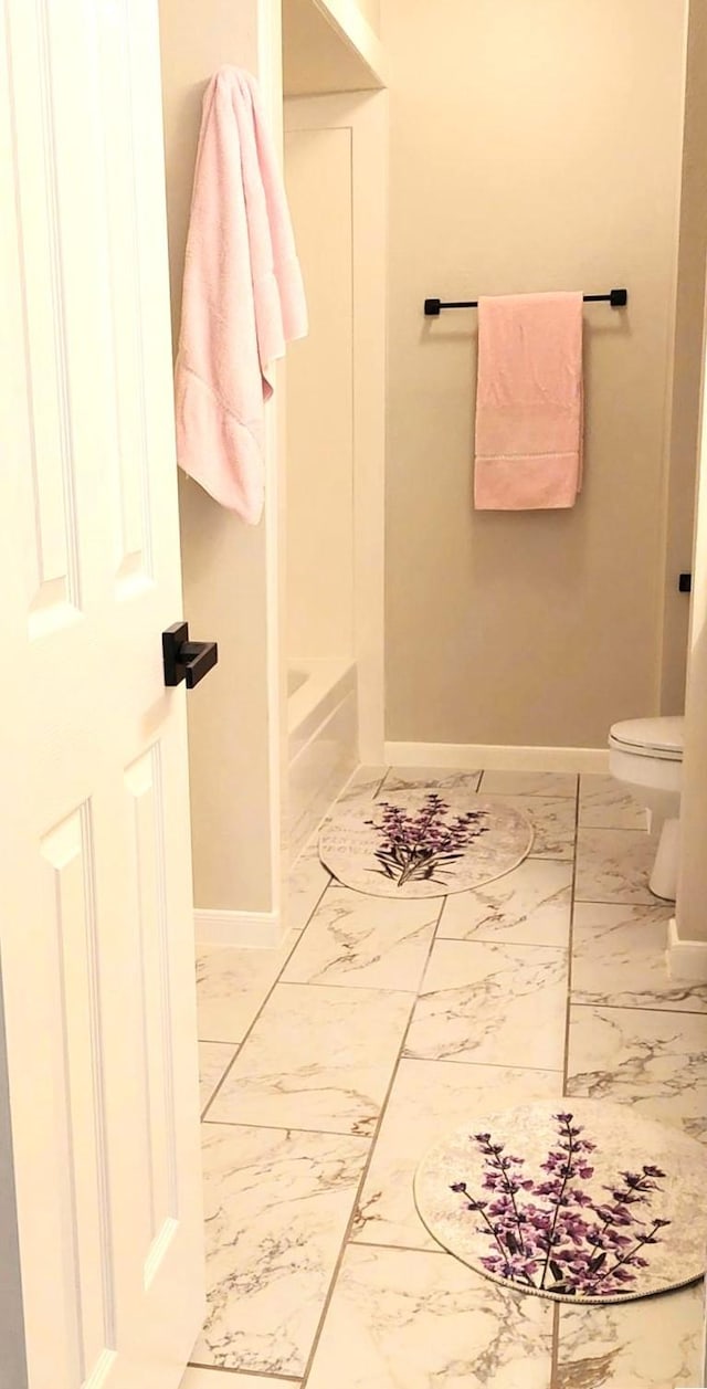 full bath featuring baseboards, toilet, marble finish floor, and a washtub