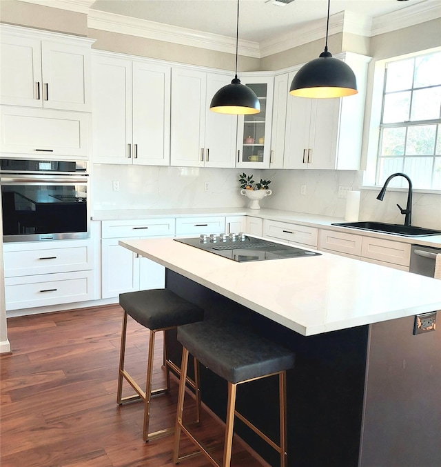 kitchen with black electric stovetop, ornamental molding, stainless steel oven, a kitchen breakfast bar, and a sink