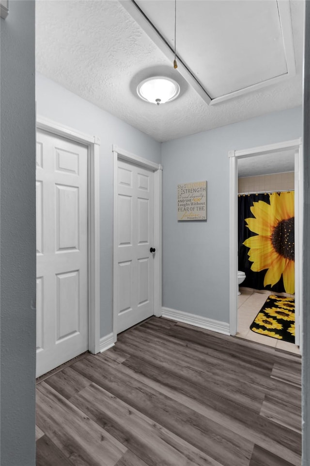 hallway with attic access, a textured ceiling, baseboards, and wood finished floors