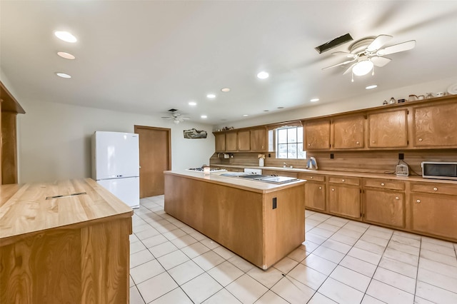 kitchen featuring light tile patterned floors, ceiling fan, a kitchen island, stainless steel microwave, and freestanding refrigerator