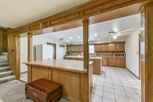 kitchen with a kitchen island, a ceiling fan, freestanding refrigerator, stainless steel microwave, and decorative columns