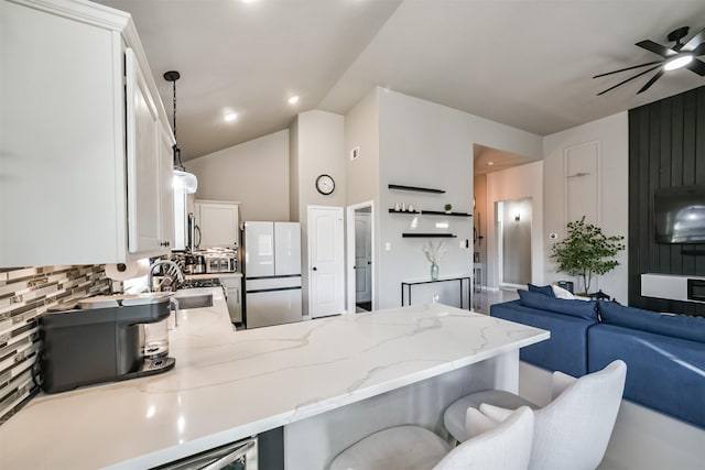 kitchen featuring a peninsula, open floor plan, decorative backsplash, freestanding refrigerator, and light stone countertops