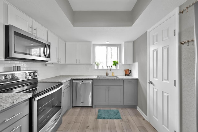 kitchen with stainless steel appliances, backsplash, gray cabinetry, light wood-style floors, and a sink