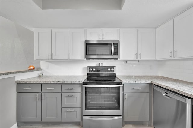 kitchen featuring light stone counters, stainless steel appliances, white cabinetry, gray cabinets, and decorative backsplash