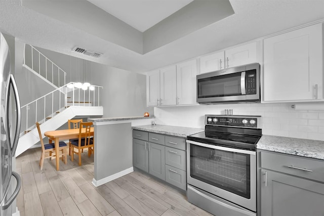 kitchen with gray cabinetry, visible vents, light wood-style floors, appliances with stainless steel finishes, and backsplash