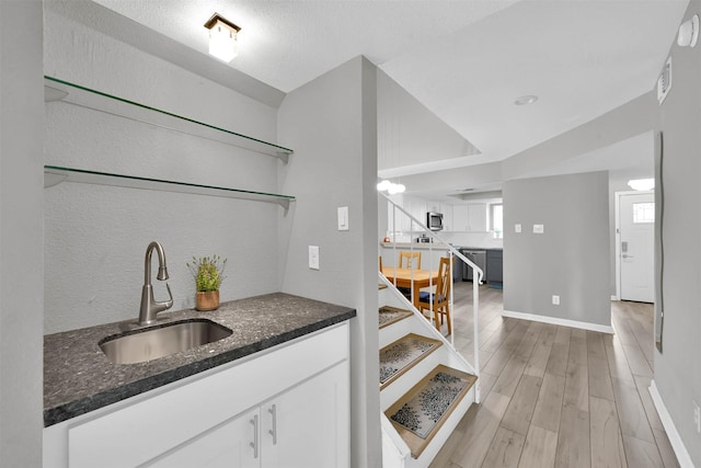 bar with baseboards, light wood-style flooring, stainless steel microwave, and a sink