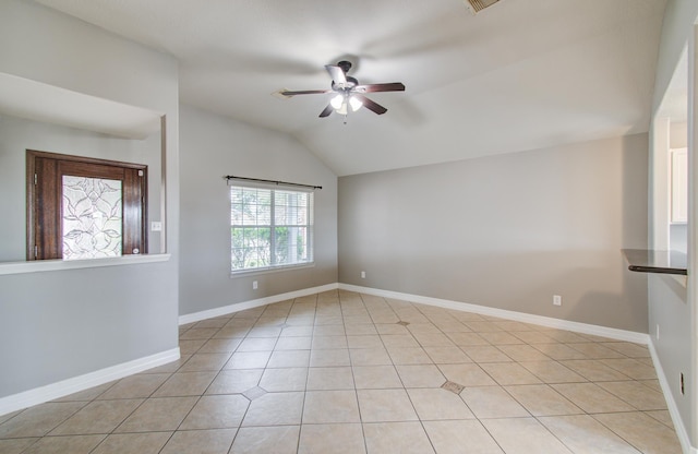 spare room with light tile patterned floors, vaulted ceiling, a ceiling fan, and baseboards