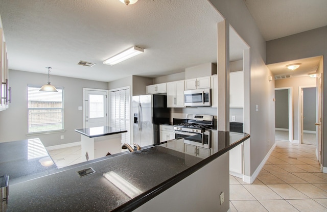 kitchen featuring light tile patterned floors, stainless steel appliances, a kitchen island, white cabinets, and dark countertops