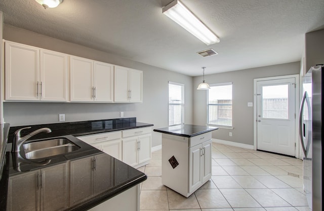 kitchen with visible vents, a center island, freestanding refrigerator, white cabinetry, and a sink