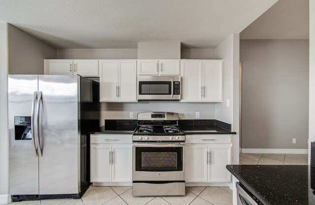 kitchen with light tile patterned floors, baseboards, white cabinets, appliances with stainless steel finishes, and dark stone counters