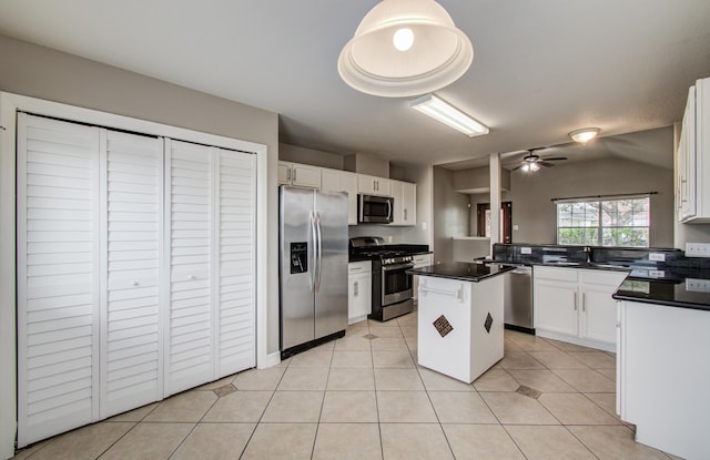 kitchen with light tile patterned floors, dark countertops, appliances with stainless steel finishes, white cabinets, and a kitchen island