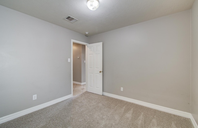 spare room featuring baseboards, visible vents, a textured ceiling, and light colored carpet