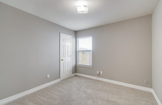 unfurnished room with light colored carpet, a textured ceiling, and baseboards