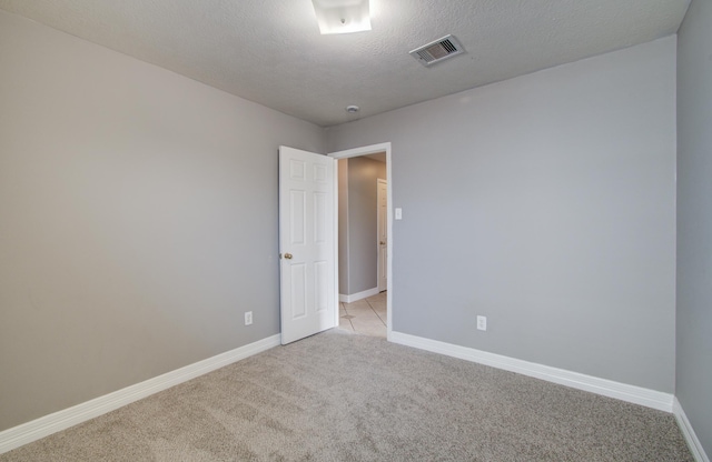 empty room featuring light carpet, baseboards, visible vents, and a textured ceiling