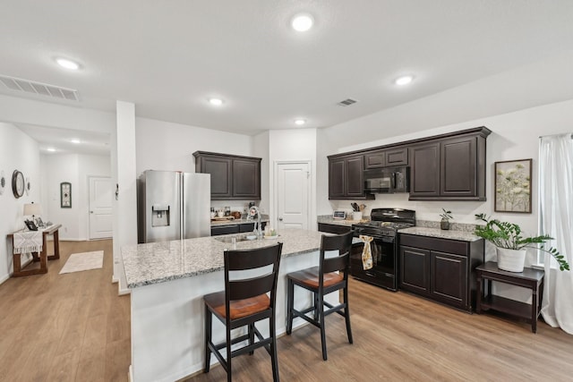 kitchen with a breakfast bar area, visible vents, light wood-style flooring, a sink, and black appliances