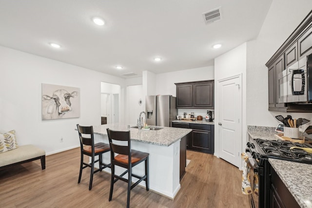 kitchen with range with gas stovetop, a breakfast bar, visible vents, light wood-type flooring, and stainless steel fridge