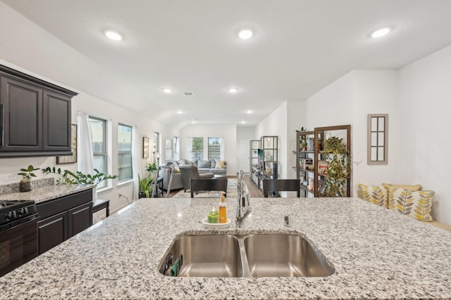 kitchen with lofted ceiling, light stone counters, recessed lighting, a sink, and gas stove