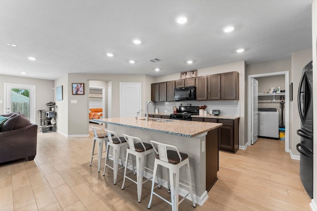 kitchen featuring visible vents, a sink, black appliances, dark brown cabinets, and a kitchen breakfast bar