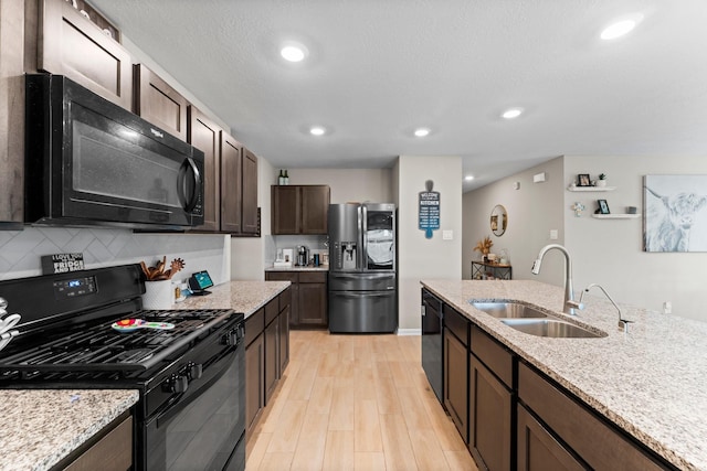 kitchen featuring dark brown cabinetry, a sink, light wood-type flooring, backsplash, and black appliances