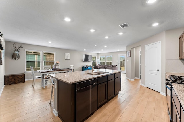 kitchen featuring visible vents, dishwasher, stainless steel gas range, a kitchen island with sink, and a sink