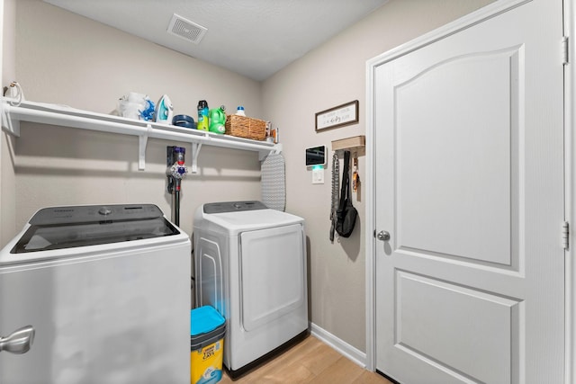 clothes washing area featuring washer and clothes dryer, light wood finished floors, visible vents, laundry area, and baseboards