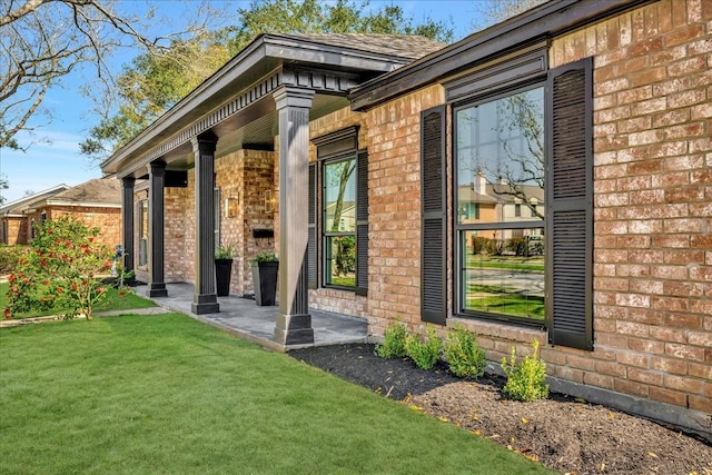 entrance to property with brick siding, a yard, and roof with shingles