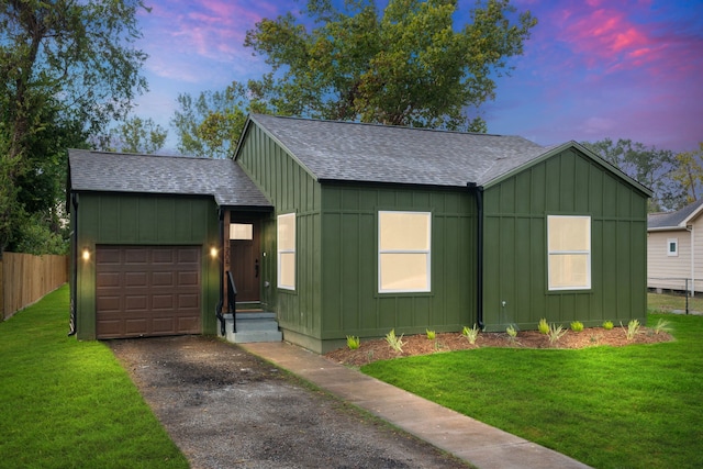 view of front of home featuring aphalt driveway, a shingled roof, a lawn, an attached garage, and board and batten siding