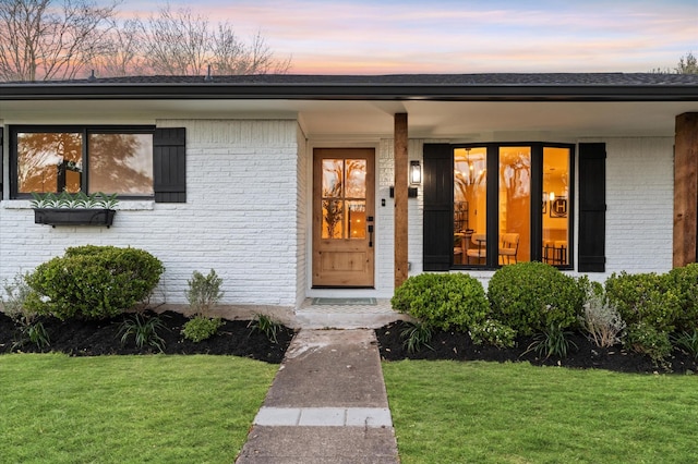 property entrance featuring a lawn and brick siding