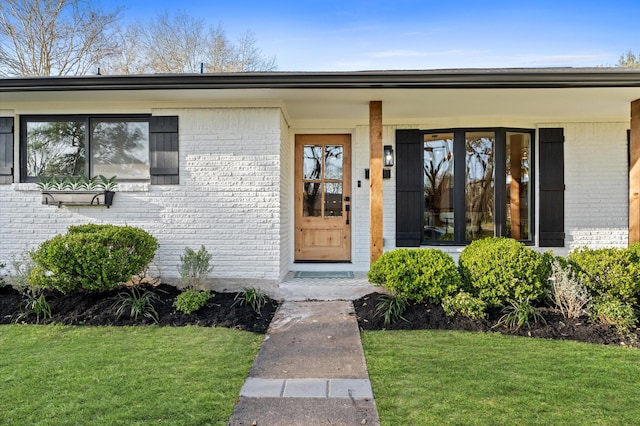 property entrance with brick siding and a lawn