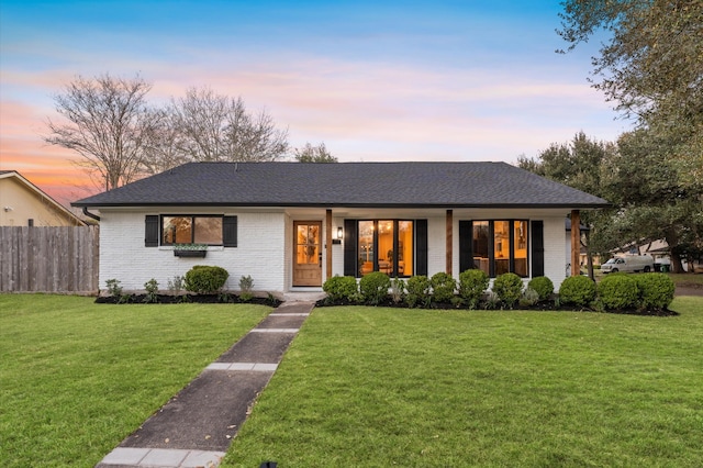 view of front of property featuring a shingled roof, a front yard, fence, and brick siding