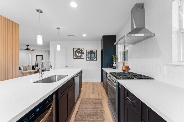 kitchen featuring stainless steel appliances, hanging light fixtures, backsplash, a sink, and wall chimney exhaust hood