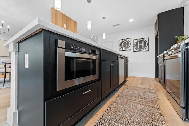 kitchen featuring light wood-style flooring, visible vents, light countertops, dark cabinetry, and pendant lighting