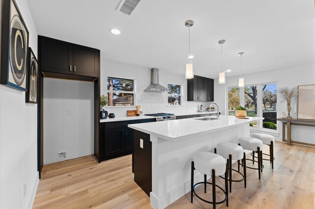 kitchen featuring visible vents, stove, light countertops, wall chimney range hood, and a sink