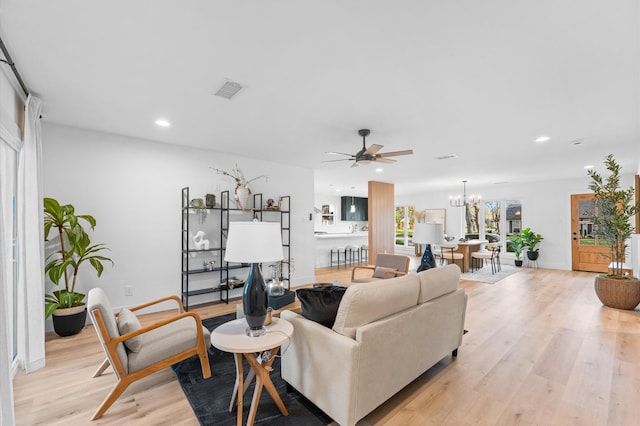 living room featuring ceiling fan with notable chandelier, recessed lighting, visible vents, and light wood-style floors