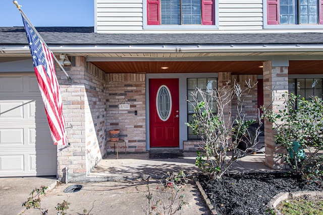 entrance to property featuring a porch, an attached garage, brick siding, and a shingled roof