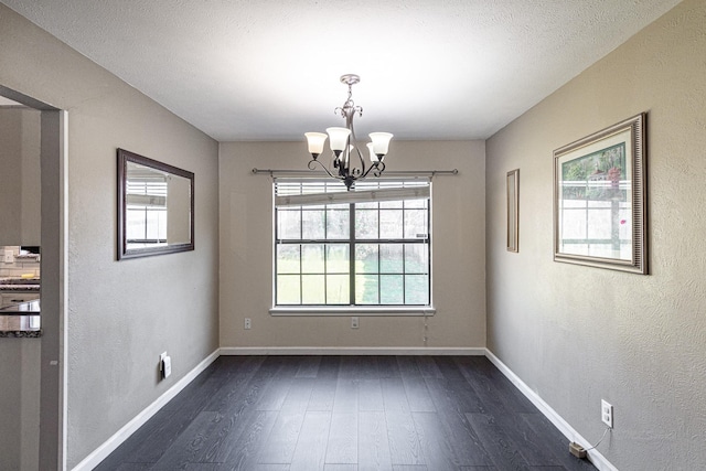 unfurnished dining area featuring dark wood-style floors, plenty of natural light, baseboards, and an inviting chandelier