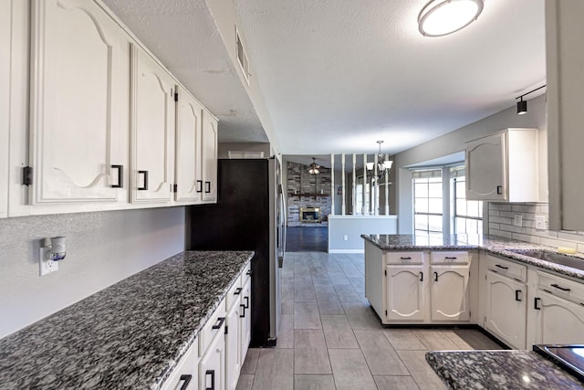 kitchen with wood finish floors, decorative backsplash, dark stone countertops, a peninsula, and white cabinets