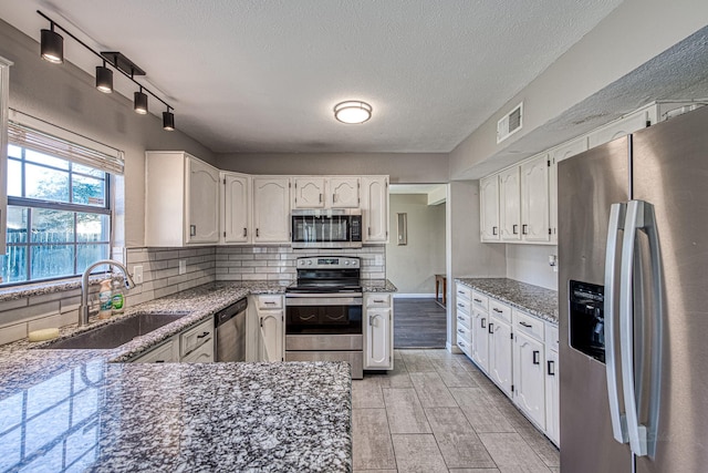 kitchen featuring visible vents, stone countertops, a sink, appliances with stainless steel finishes, and backsplash