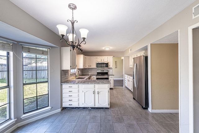 kitchen with a sink, tasteful backsplash, appliances with stainless steel finishes, white cabinets, and a chandelier