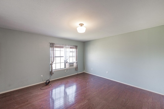 unfurnished room with cooling unit, a textured ceiling, baseboards, and wood finished floors