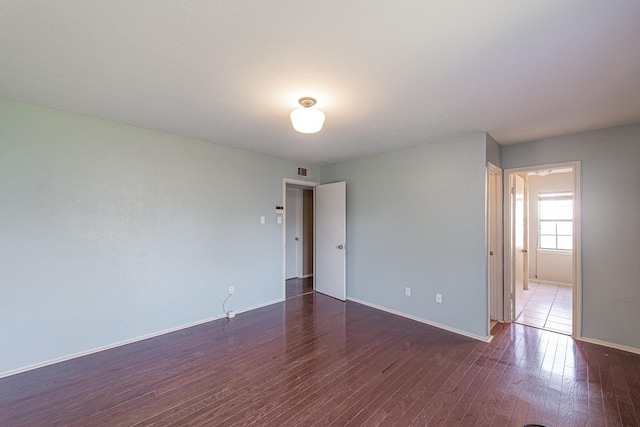 spare room featuring visible vents, baseboards, and dark wood-type flooring