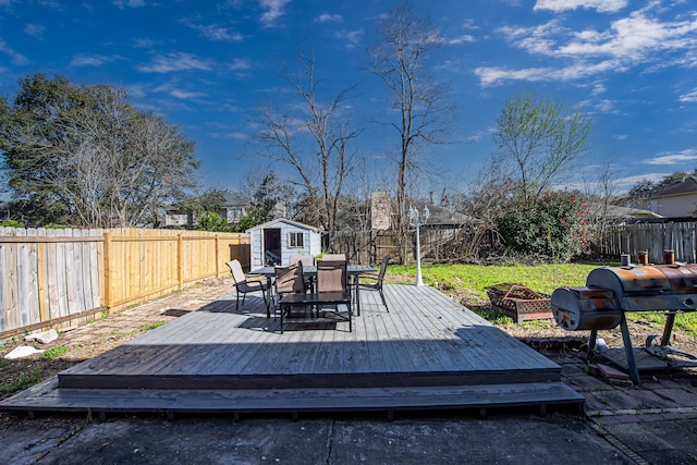 wooden terrace with outdoor dining space, an outdoor structure, a fenced backyard, and an outdoor fire pit