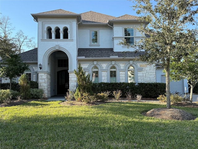 view of front facade with a shingled roof, a front yard, stone siding, and stucco siding