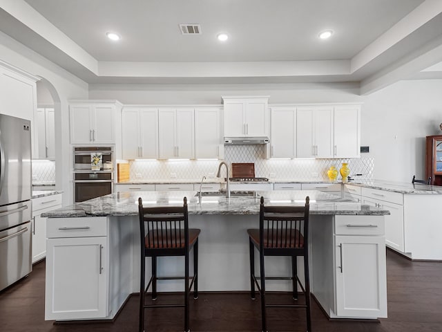 kitchen featuring visible vents, a sink, white cabinets, stainless steel appliances, and a kitchen island with sink