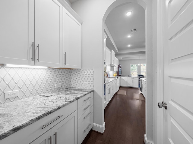 kitchen featuring light stone counters, dark wood finished floors, arched walkways, and white cabinetry