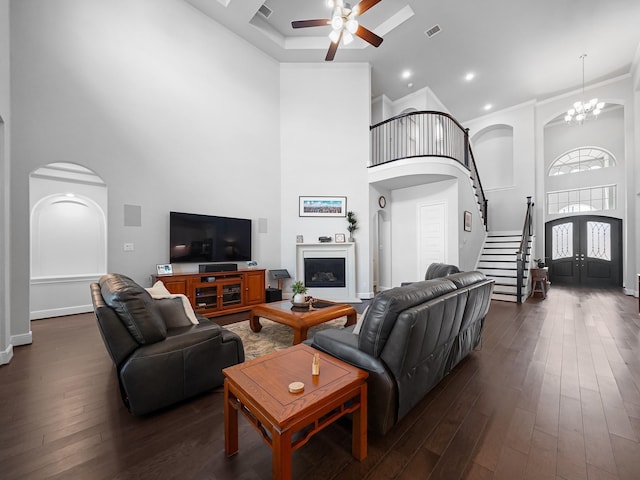 living area featuring dark wood-style floors, ceiling fan with notable chandelier, and a high ceiling