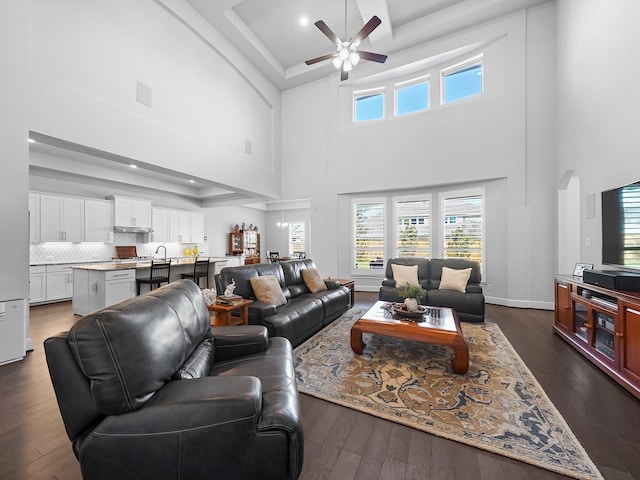 living area featuring visible vents, arched walkways, ceiling fan, dark wood-type flooring, and a raised ceiling